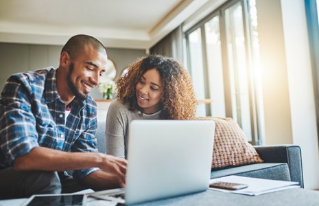 Smiling couple reviewing paperwork on a laptop